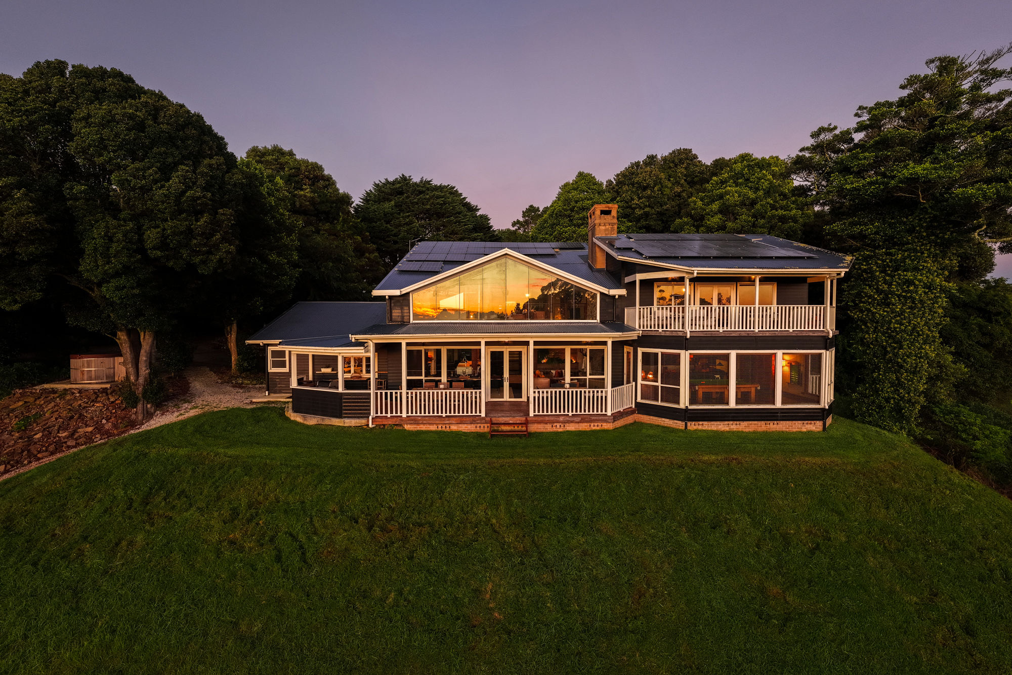 Wildefell Estate at twilight, the lit house on its lawn with the escarpment behind.